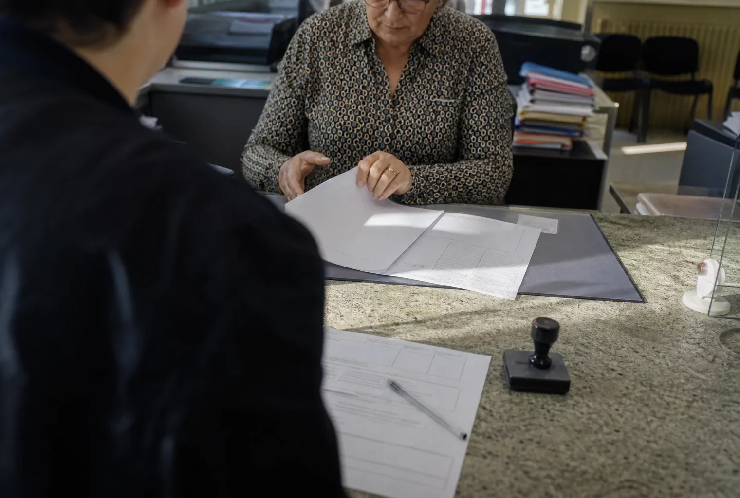 Des formulaires de parrainage posés sur un comptoir de mairie, avec un stylo et un tampon administratif.