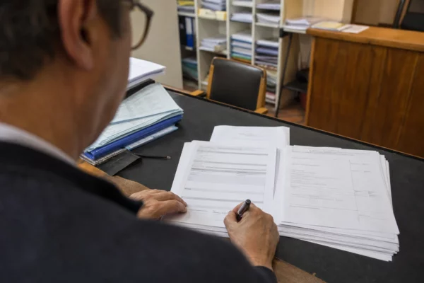 Des formulaires de parrainage sont signés dans un bureau de mairie, avec des dossiers et du matériel administratif.