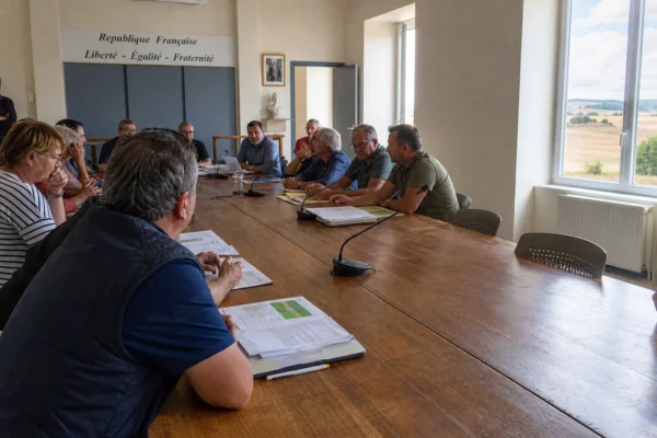 Réunion agricole dans une salle municipale française, avec dossiers, micros et une chaise vide autour d’une table