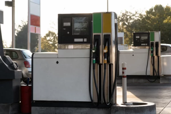 Une pompe à carburant en station-service, avec affichage des prix et une voiture en train de faire le plein.