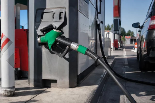 Pompe à carburant verte d’une station-service française, en gros plan, avec autres pompes floues et soleil de fin de matinée.