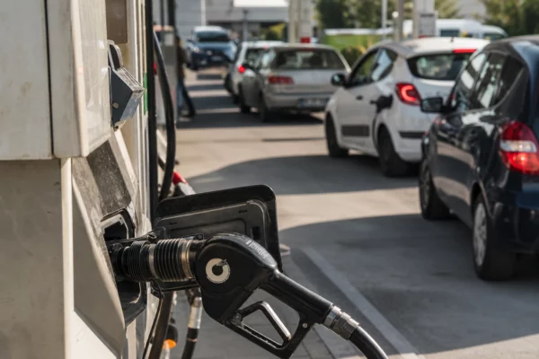 Pompe à carburant usée au premier plan d’une station française, avec voitures en file d’attente derrière.