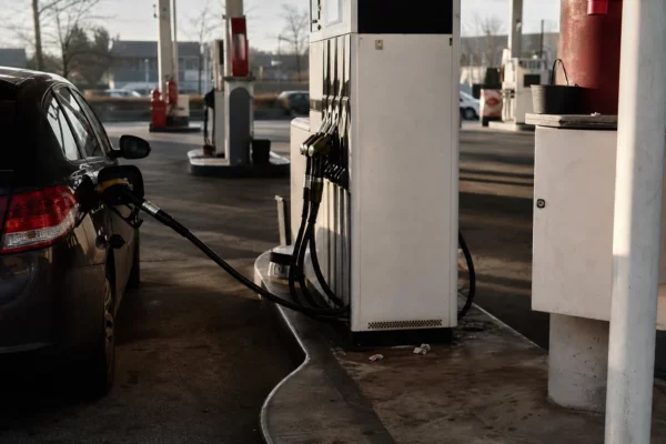Une voiture attend à une station-service, près d’une pompe à carburant, sur fond d’aire de ravitaillement.