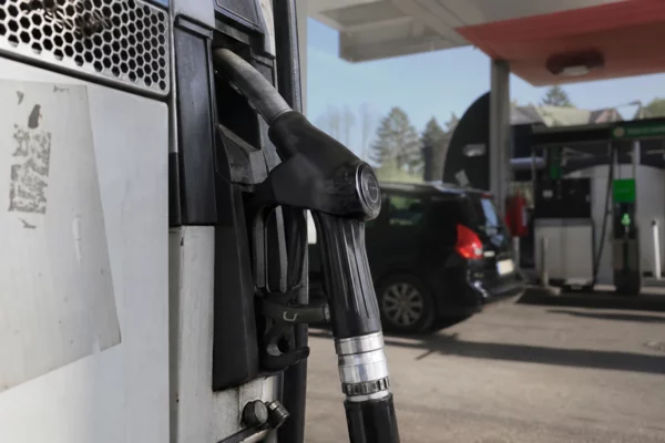 Une pompe à carburant en station-service, avec une voiture en arrière-plan et le prix affiché sur la borne.