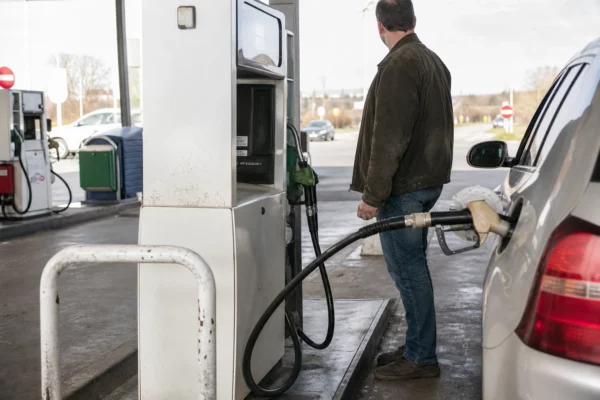 Automobiliste faisant le plein à une pompe en station-service de grande route, avec aire et autres pompes en arrière-plan.