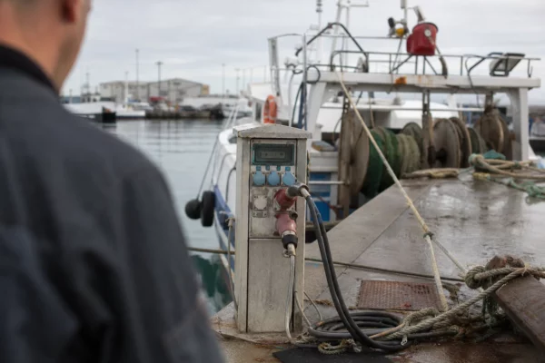 Dans un port de pêche, une borne d’alimentation à quai et des câbles près de bateaux amarrés.