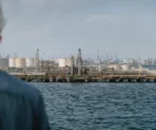 Vue large d’un terminal pétrolier à Yanbu, avec quais, cuves, grues portuaires et mer sous une lumière diffuse.