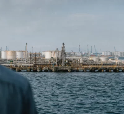Vue large d’un terminal pétrolier à Yanbu, avec quais, cuves, grues portuaires et mer sous une lumière diffuse.