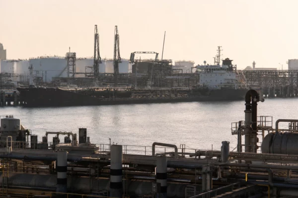 Port pétrolier de Yanbu avec tanker, pipelines et grues de chargement sous une lumière de contre-jour dure.