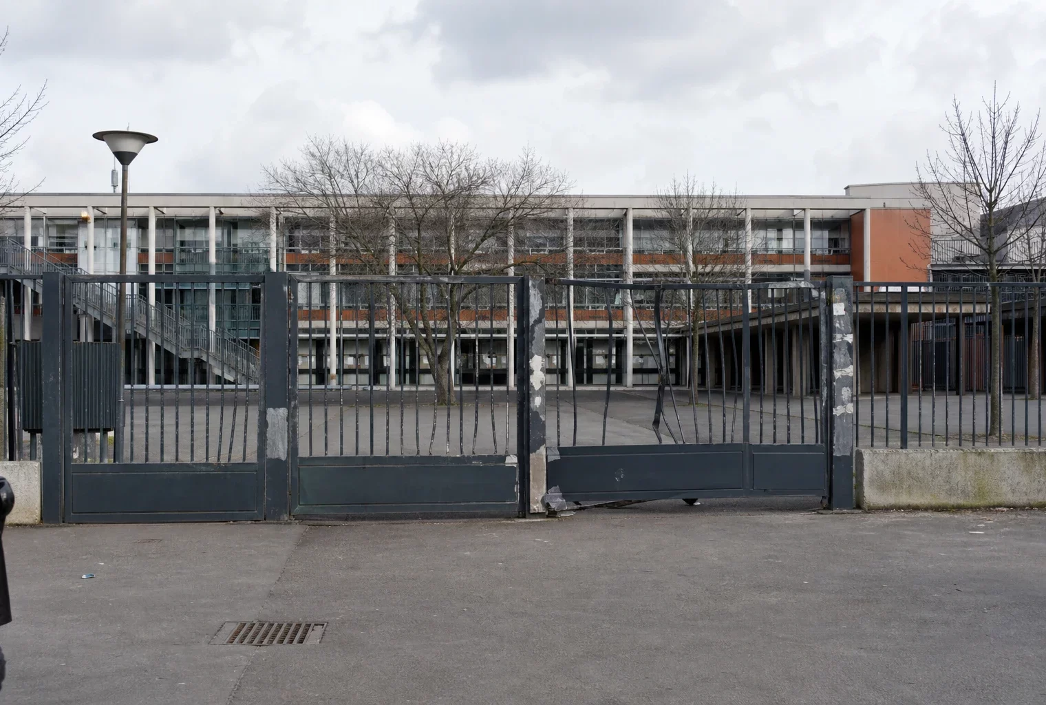 Portail de lycée abîmé devant un établissement francilien, avec traces de réparation et cour en arrière-plan.