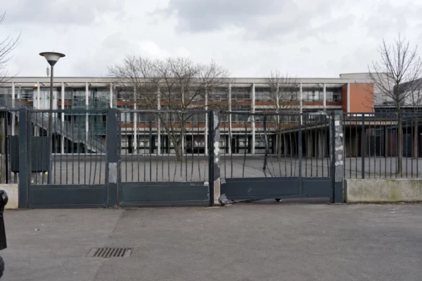 Portail de lycée abîmé devant un établissement francilien, avec traces de réparation et cour en arrière-plan.
