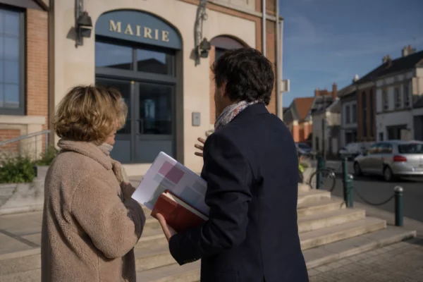Élu local anonyme avec un carnet devant une mairie française, lors d’un échange de terrain en campagne politique