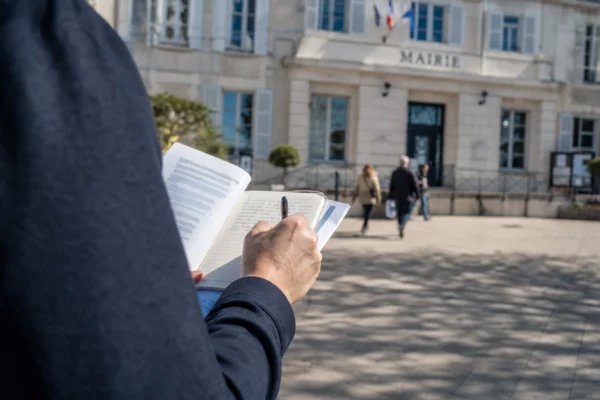 Élu local anonyme prenant des notes devant une mairie française, dans une lumière naturelle de fin de journée