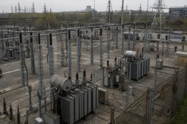 Sous-station électrique en Ukraine, clôture grillagée, transformateurs et pylônes sous une lumière diffuse grise.