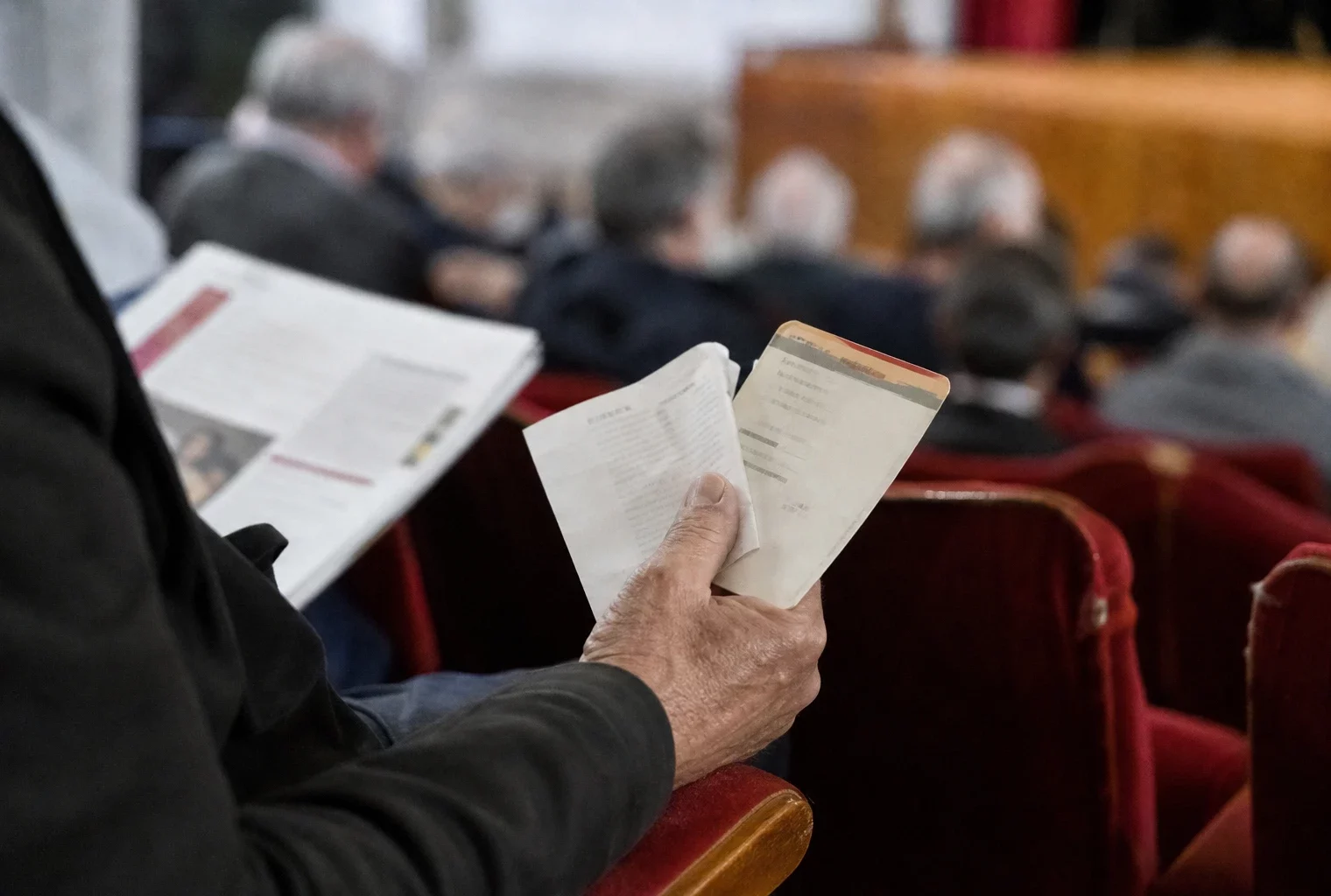 Main tenant un ticket et un reçu de carburant sur le fauteuil usé d’une salle culturelle française