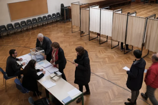 Un bureau de vote de primaire avec isoloirs, table d’émargement et bulletins, dans une salle municipale.