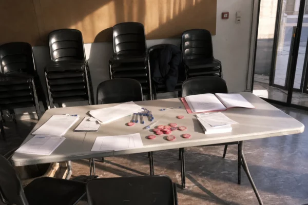 Table d’enregistrement de candidatures dans un local de parti, avec dossiers ouverts et chaises vides.