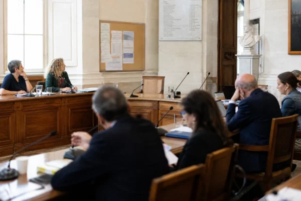 Salle de conseil municipal française avec une chaise vide, des micros et des dossiers avant un débat politique