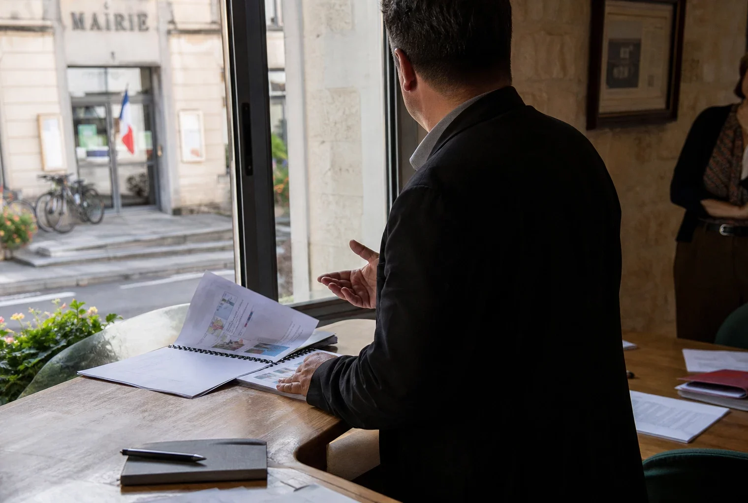 Élu local anonyme consultant un dossier dans une mairie française, avec une rue en arrière-plan