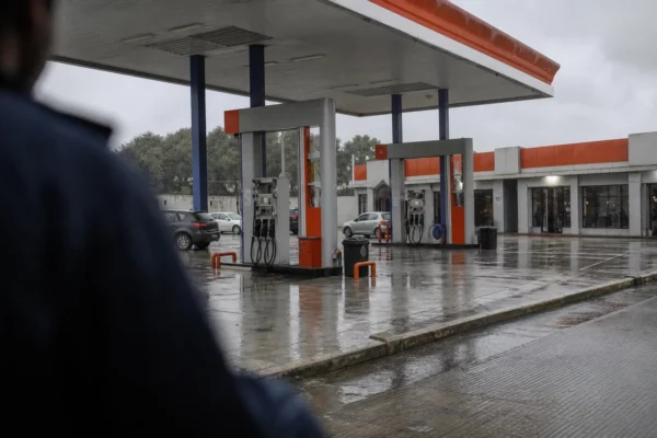 Station-service française sous la pluie, pompes à carburant et véhicules en attente, reflets humides sur l’aire vide.
