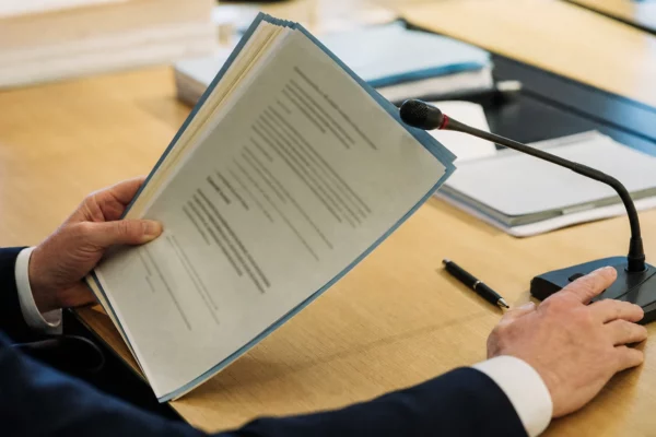 Mains anonymes tenant un dossier de nomination près d’un micro de commission dans une salle de justice française