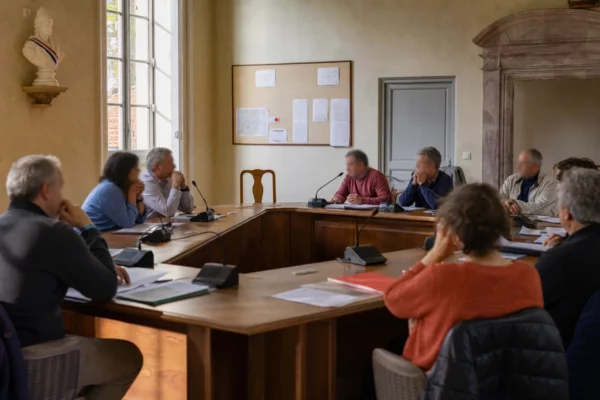 Réunion d’un conseil municipal français avec une chaise vide, des micros et des dossiers sur une table en bois
