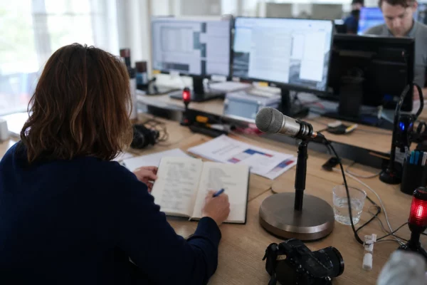 Journaliste préparant un sujet sur le périscolaire parisien dans une rédaction française, avec carnet et micro sans logo