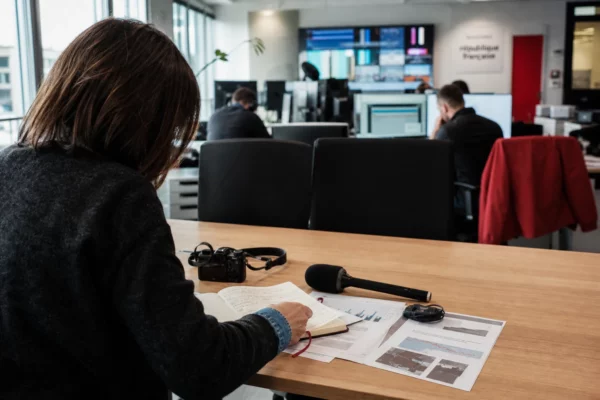 Rédaction française préparant un sujet sur l’avenir de l’industrie automobile, avec carnet, micro et écrans abstraits