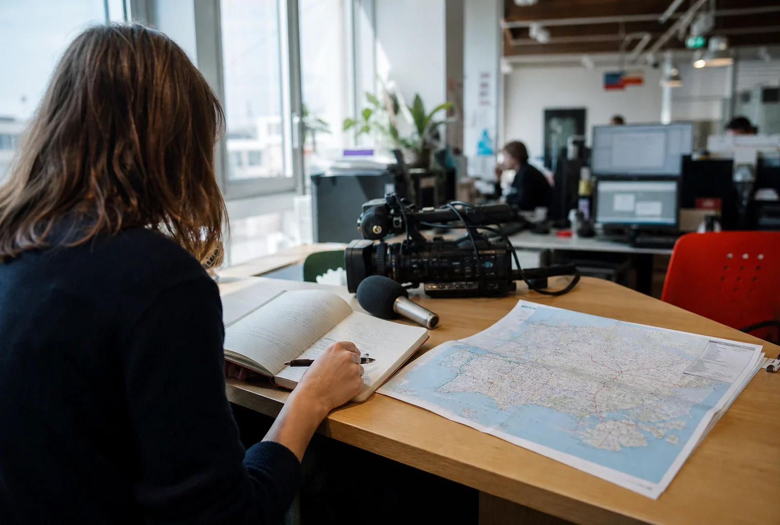Journaliste préparant un sujet politique dans une rédaction française, avec carnet, carte papier floue et micro de presse