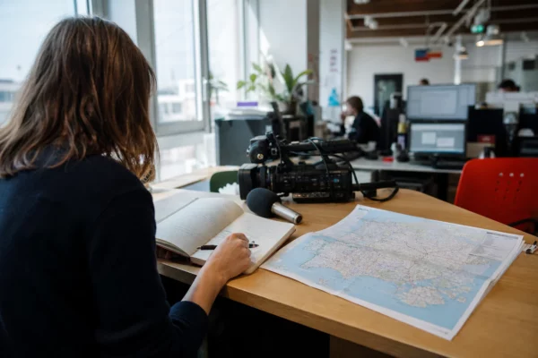 Journaliste préparant un sujet politique dans une rédaction française, avec carnet, carte papier floue et micro de presse