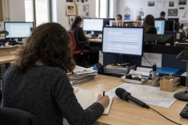 Journaliste préparant un sujet budgétaire dans une rédaction locale française, avec carnet, micro et carte floue