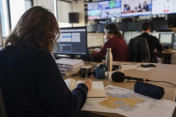 Journaliste préparant un sujet politique dans une rédaction locale, avec carnet, carte floue et micro sans logo