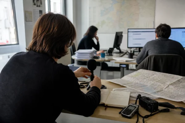 Journaliste préparant un sujet sur la présidentielle 2027 dans une rédaction locale française, avec carnet et carte floue