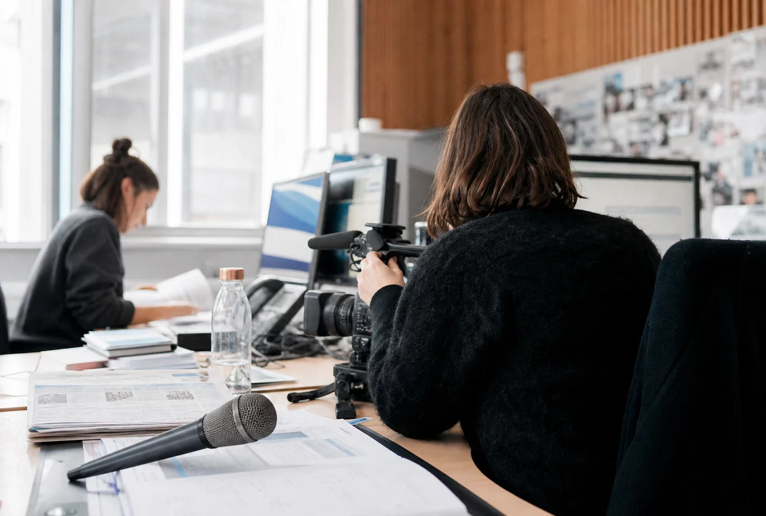 Journaliste préparant un reportage judiciaire dans une rédaction française, avec caméra, micro et écrans flous
