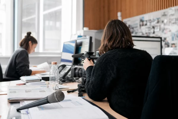 Journaliste préparant un reportage judiciaire dans une rédaction française, avec caméra, micro et écrans flous