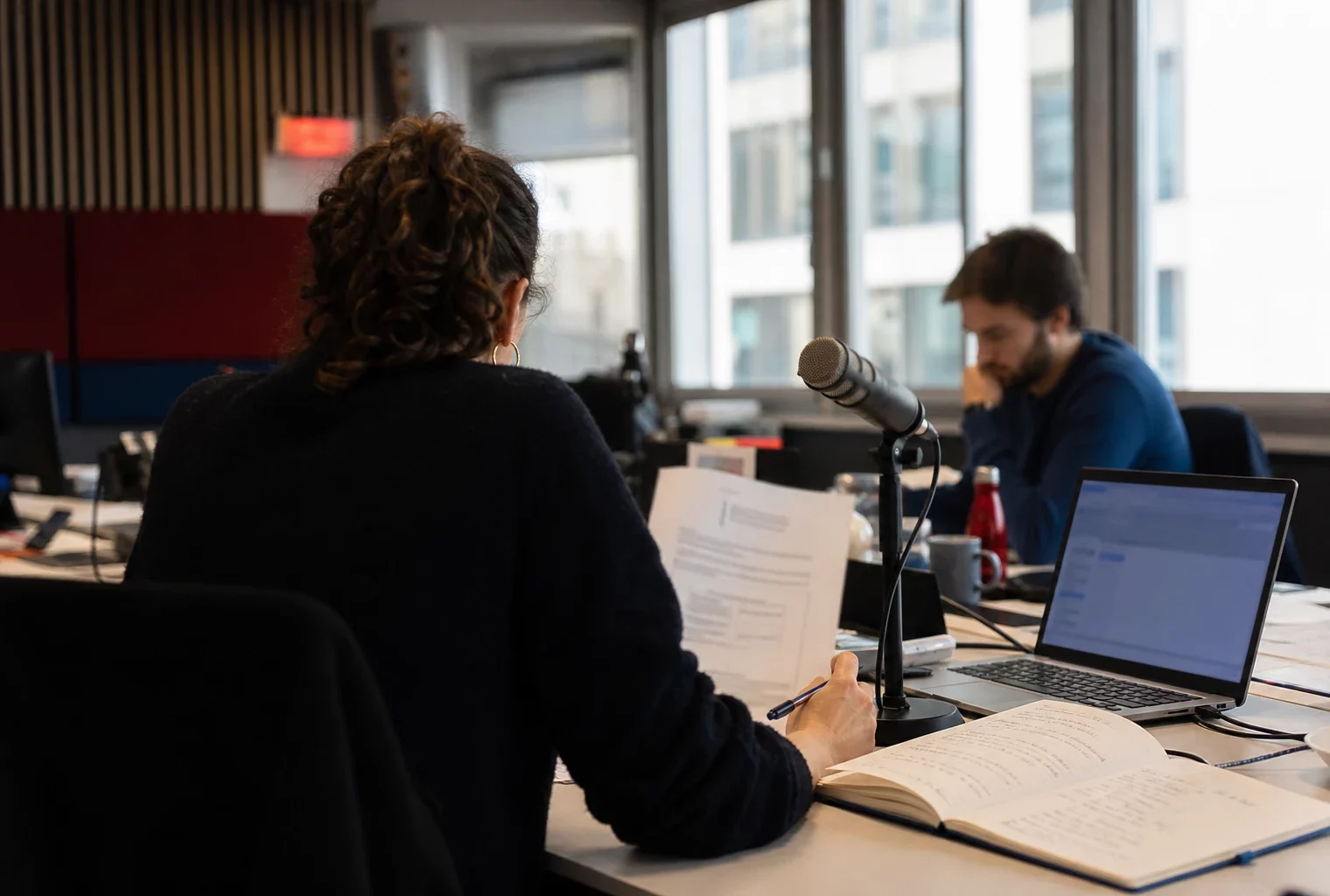 Rédaction française préparant un sujet sur la transition présidentielle, avec carnet, micro et écran abstrait