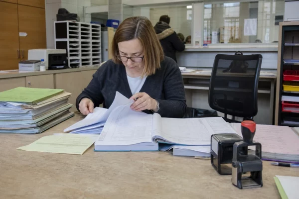Des registres administratifs de procurations dans un bureau de préfecture, avec dossiers et formulaires ouverts.