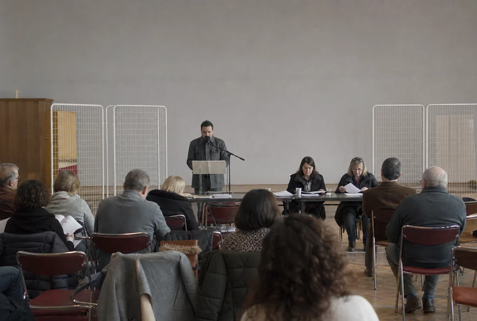 Salle de réunion de campagne avec chaises pliantes, pupitre et tracts, dans une ville moyenne française.