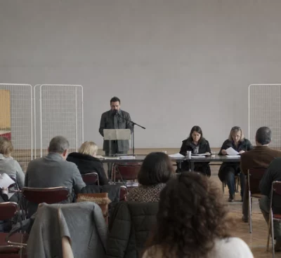 Salle de réunion de campagne avec chaises pliantes, pupitre et tracts, dans une ville moyenne française.