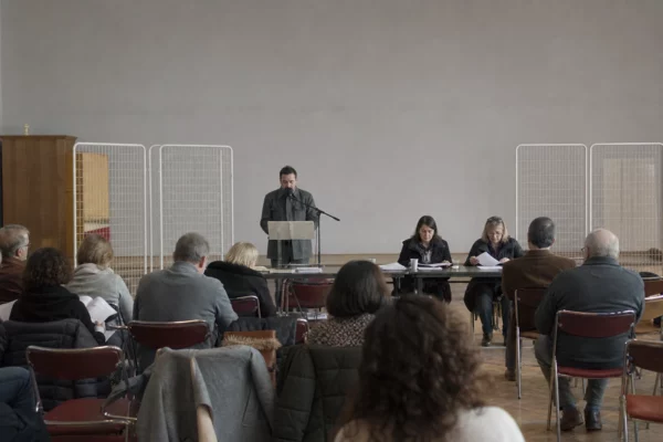 Salle de réunion de campagne avec chaises pliantes, pupitre et tracts, dans une ville moyenne française.