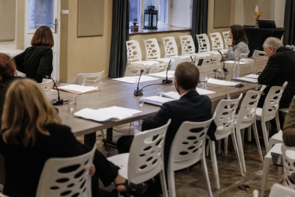 Salle de réunion à l’Assemblée nationale avec table, micros, dossiers et verres d’eau, ambiance de travail et sièges en arrière-plan.