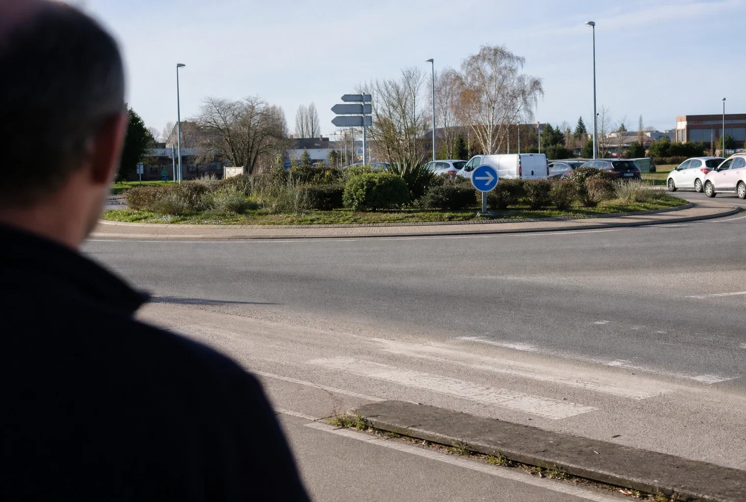 Un rond-point de zone périurbaine en France, avec chaussée circulaire, panneaux routiers et îlot central.