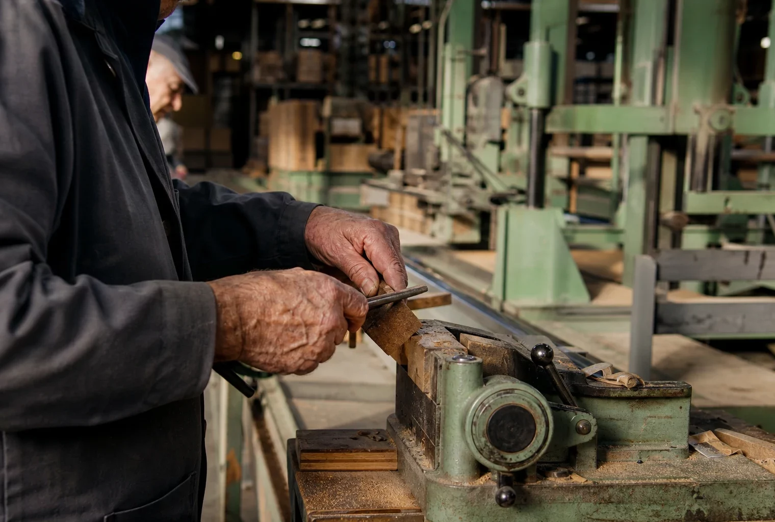 Mains de salariés âgés en atelier industriel français, sur fond de machines et rayonnages, lumière d’hiver rasante.