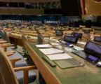 Salle de l’Assemblée générale de l’ONU à New York, rangées de pupitres, micros et dossiers sous une lumière diffuse.