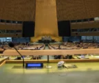 La salle de l’Assemblée générale de l’ONU avec les pupitres des délégués et la tribune au centre.
