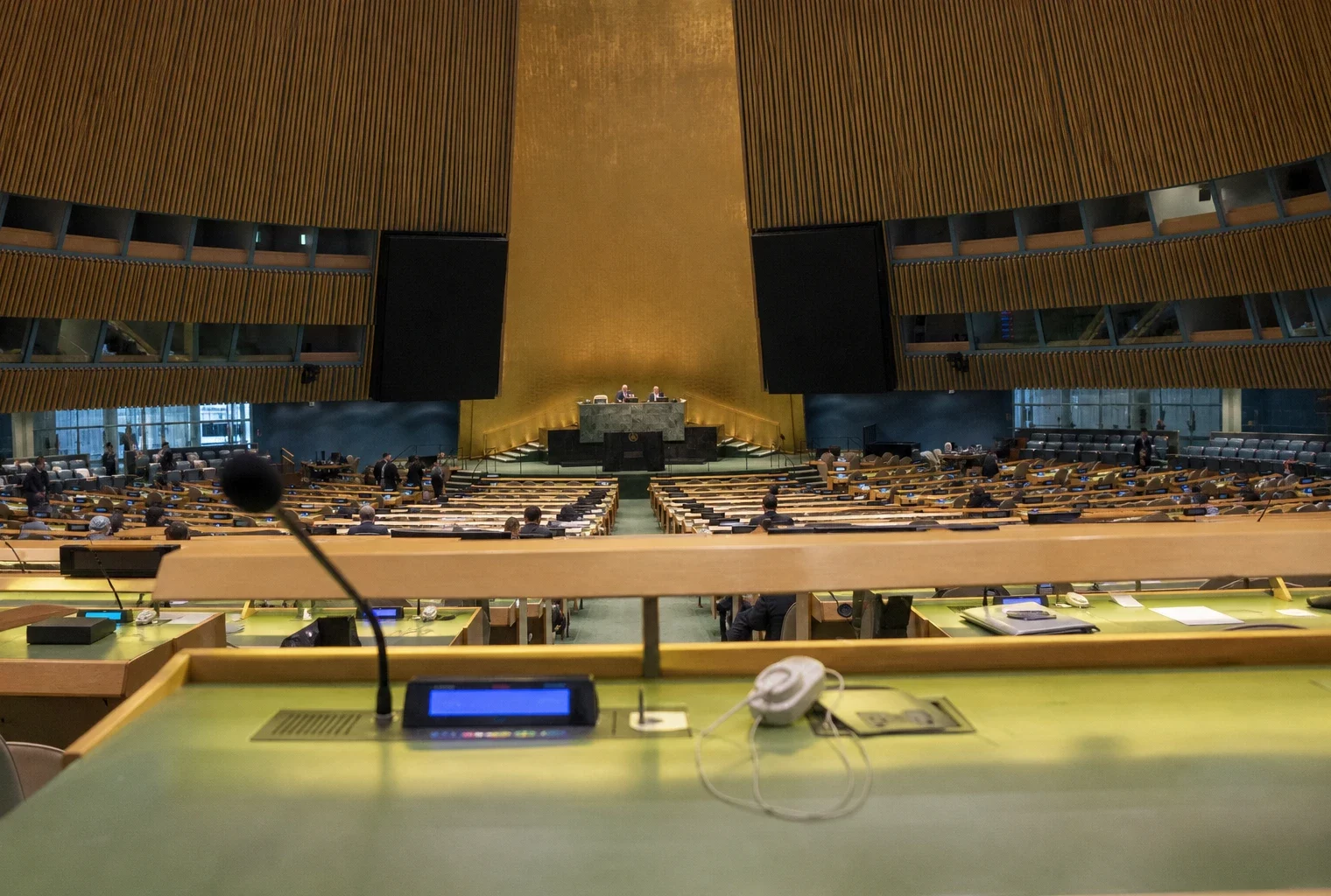 La salle de l’Assemblée générale de l’ONU avec les pupitres des délégués et la tribune au centre.