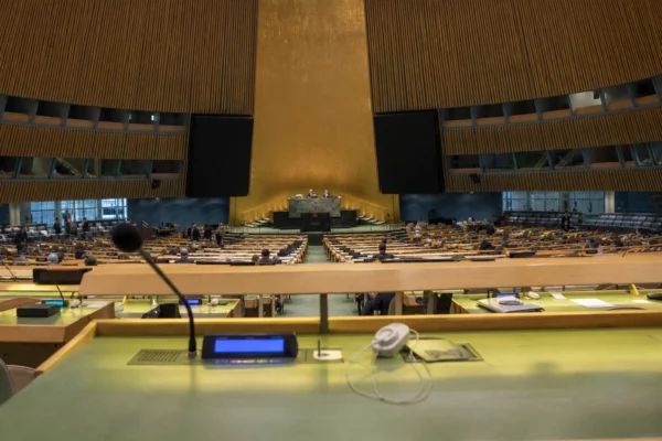 La salle de l’Assemblée générale de l’ONU avec les pupitres des délégués et la tribune au centre.
