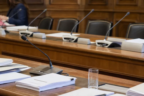 Salle de réunion du Palais du Luxembourg, table en bois, micros et dossiers vierges sous une lumière de fin de matinée.