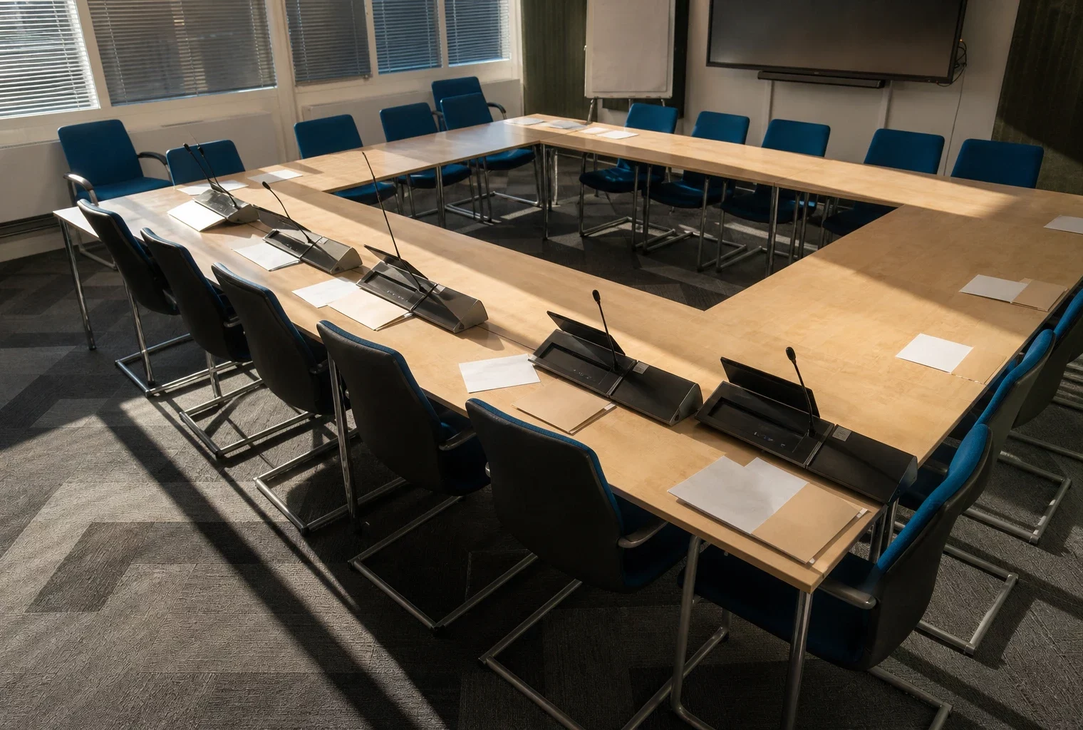 Salle de commission du Sénat à Paris, vue plongeante sur une table de réunion, pupitres, micros et dossiers laissés en place.