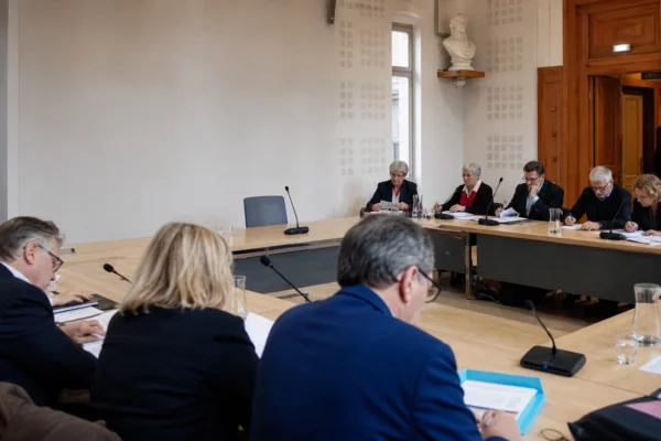Salle de conseil municipal française avec une chaise vide, des micros et des dossiers lors d’un débat budgétaire